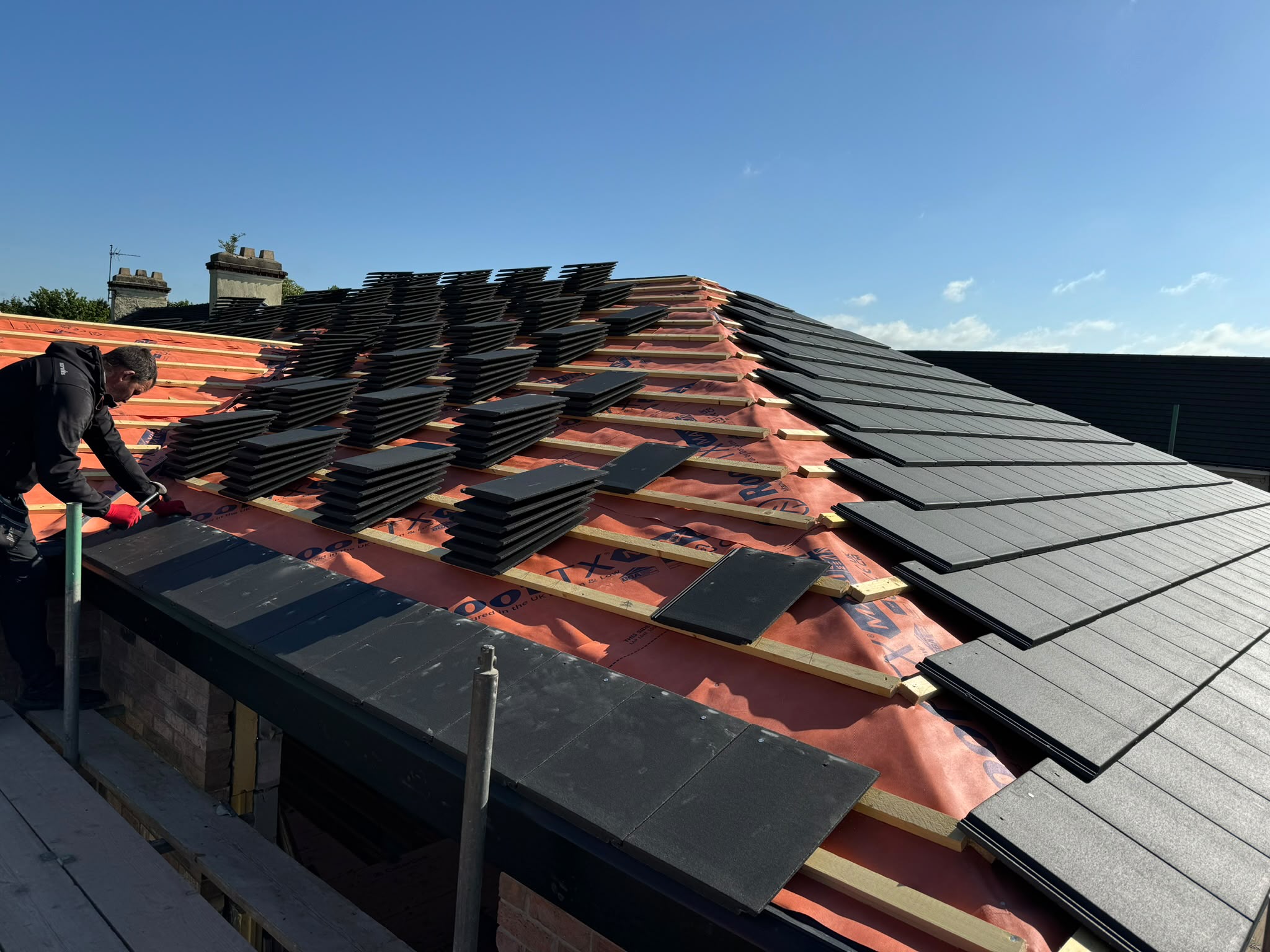 Roofer laying charcoal roof tiles on breathable membrane